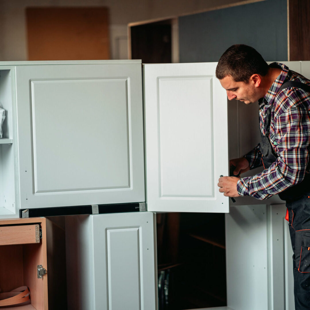 Furniture designer working on a project in a workshop Man assembling white kitchen cabinets indoors.