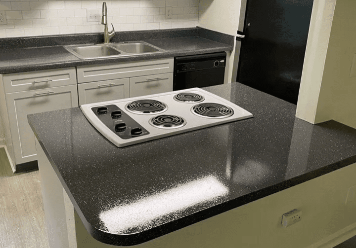 Hero A modern kitchen countertop with an electric stove top inset and a stainless steel sink in the background.